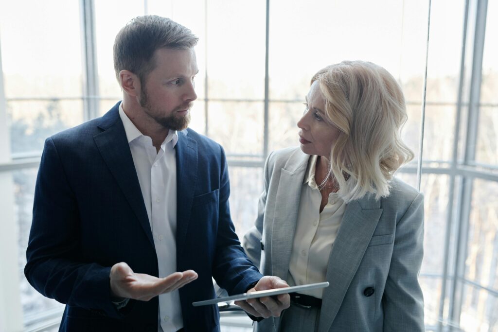 pexels-photo-7109177-7109177 Two business professionals engaged in a discussion with a tablet in a corporate setting.